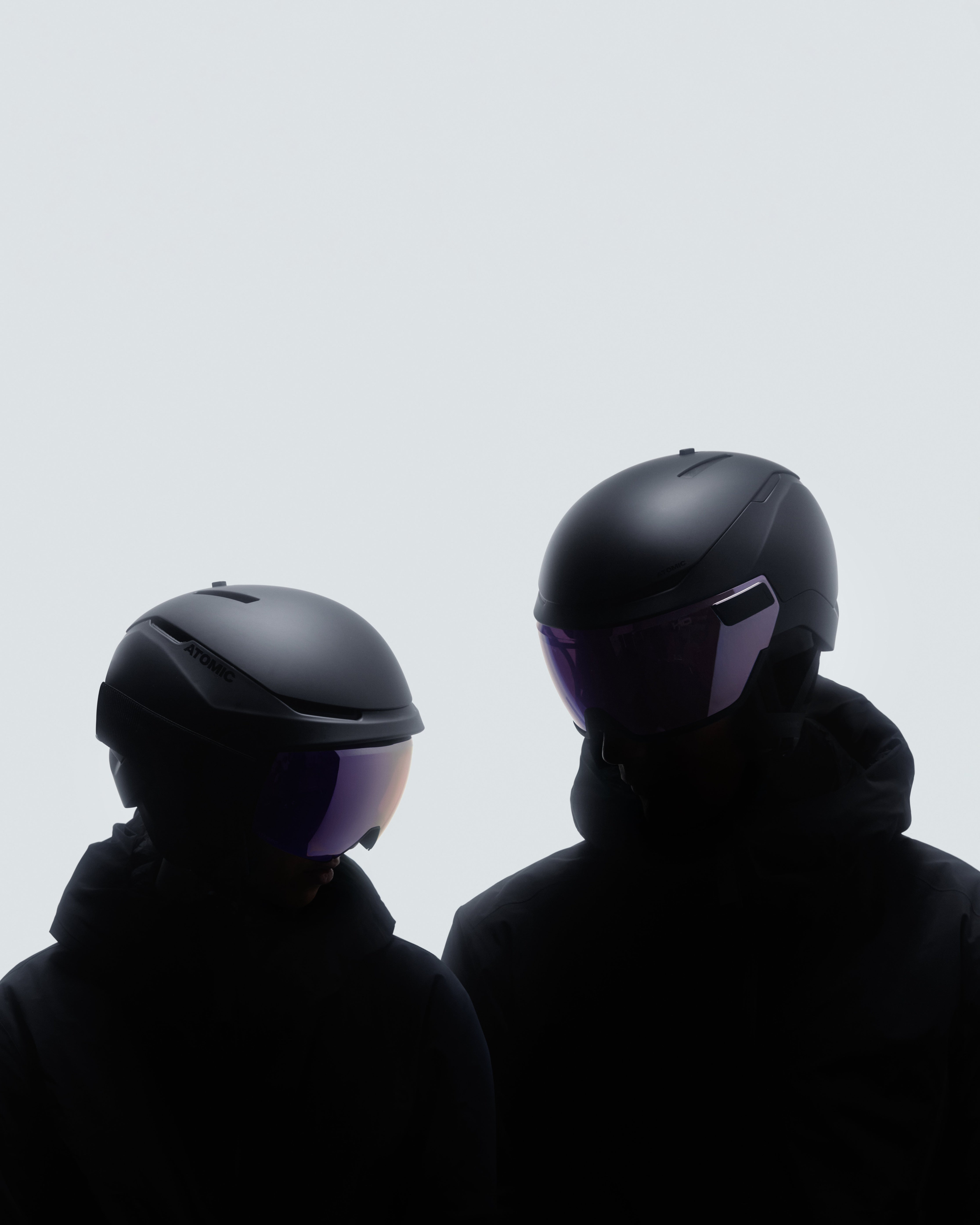 Portrait photo of two people wearing a black Atomic Revent AMID helmet with a white background.  