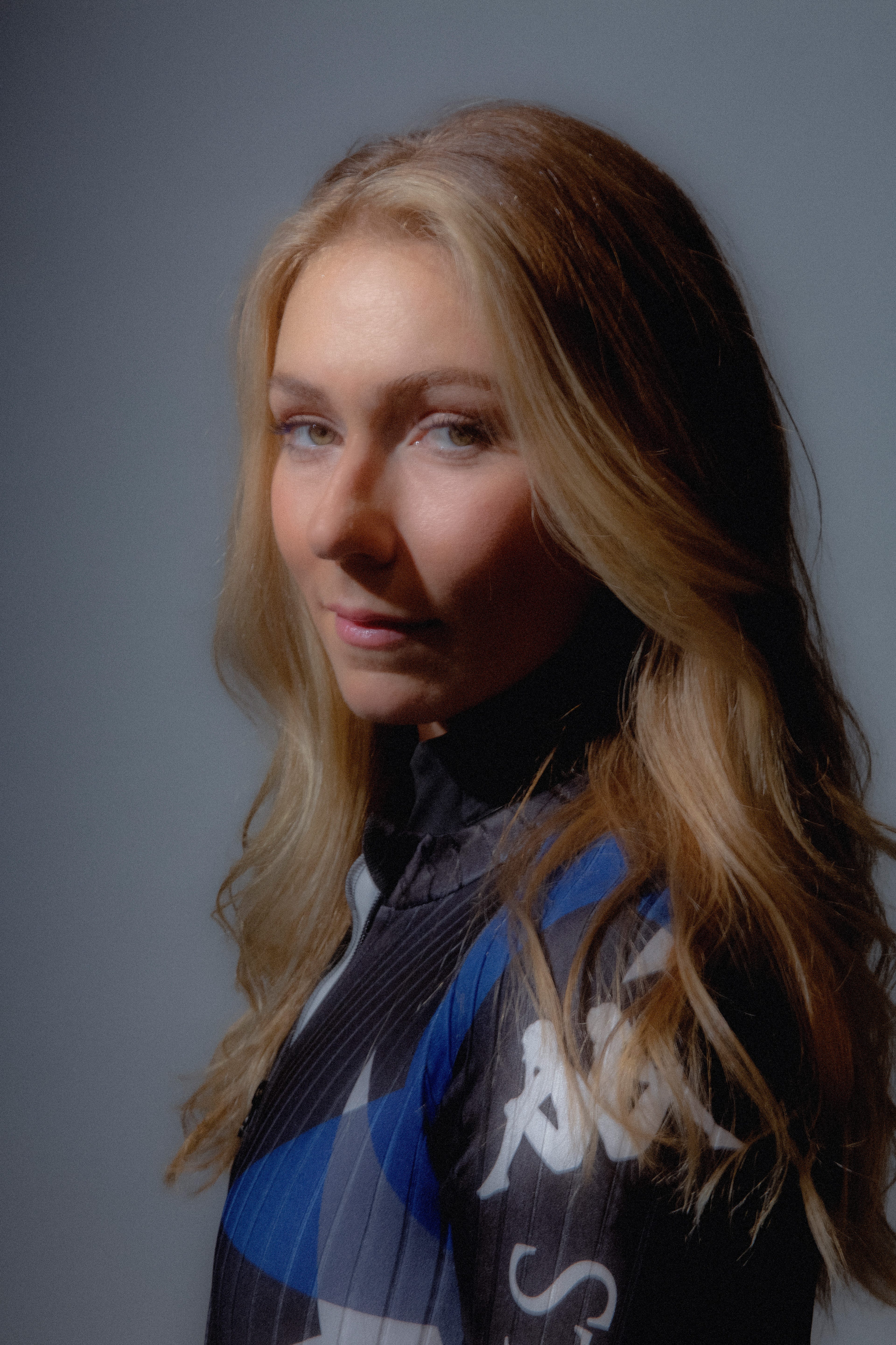 Mikaela Shiffrin in a professional studio setting, seated and facing the camera under soft studio lighting. The alpine ski champion appears relaxed and confident against a clean, modern backdrop, with production equipment and interview elements visible in the studio environment.  Provide your feedback on BizChat