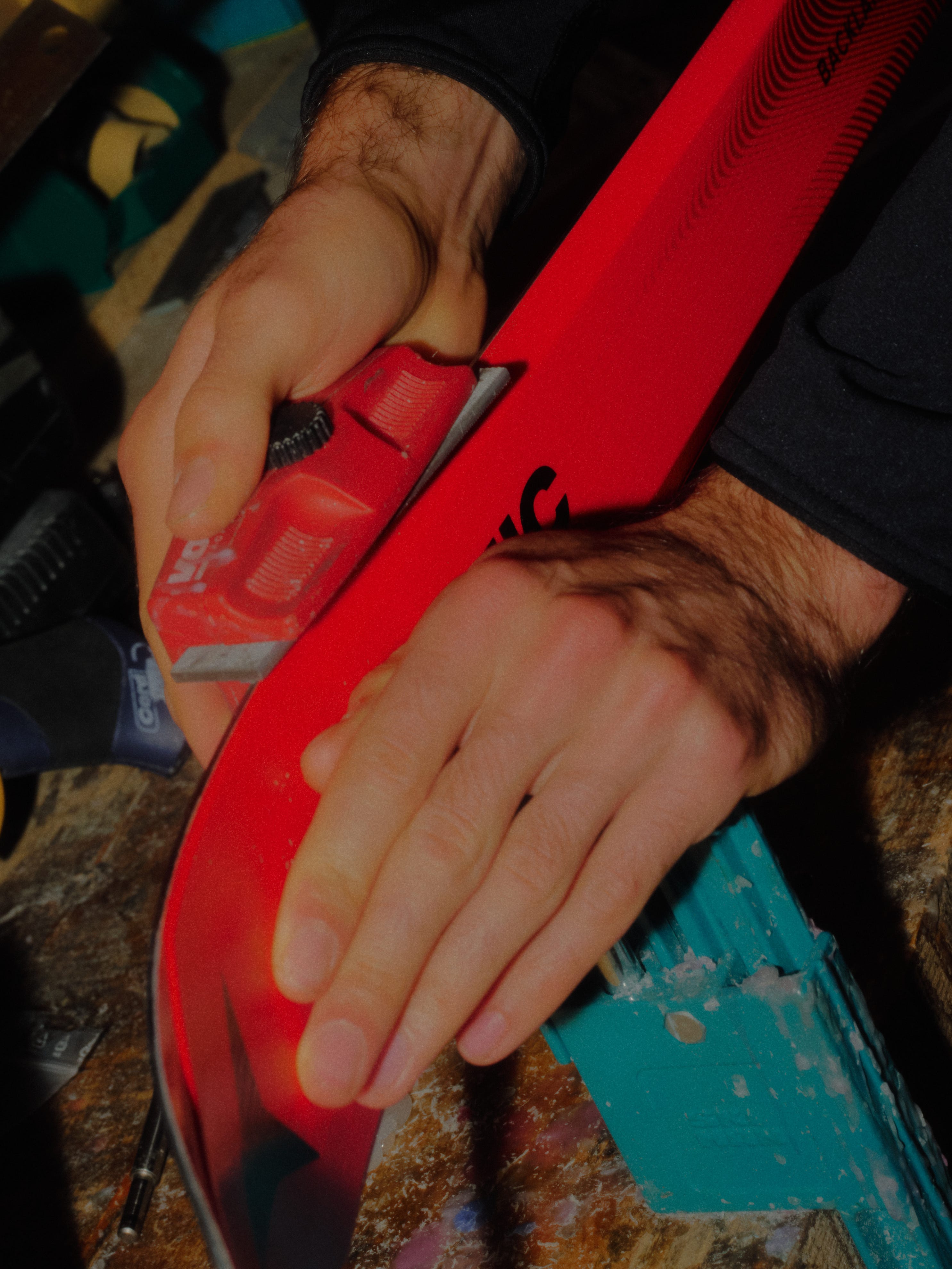 Close-up of a person's hands using a red ski base file to smooth the base of a red ski.