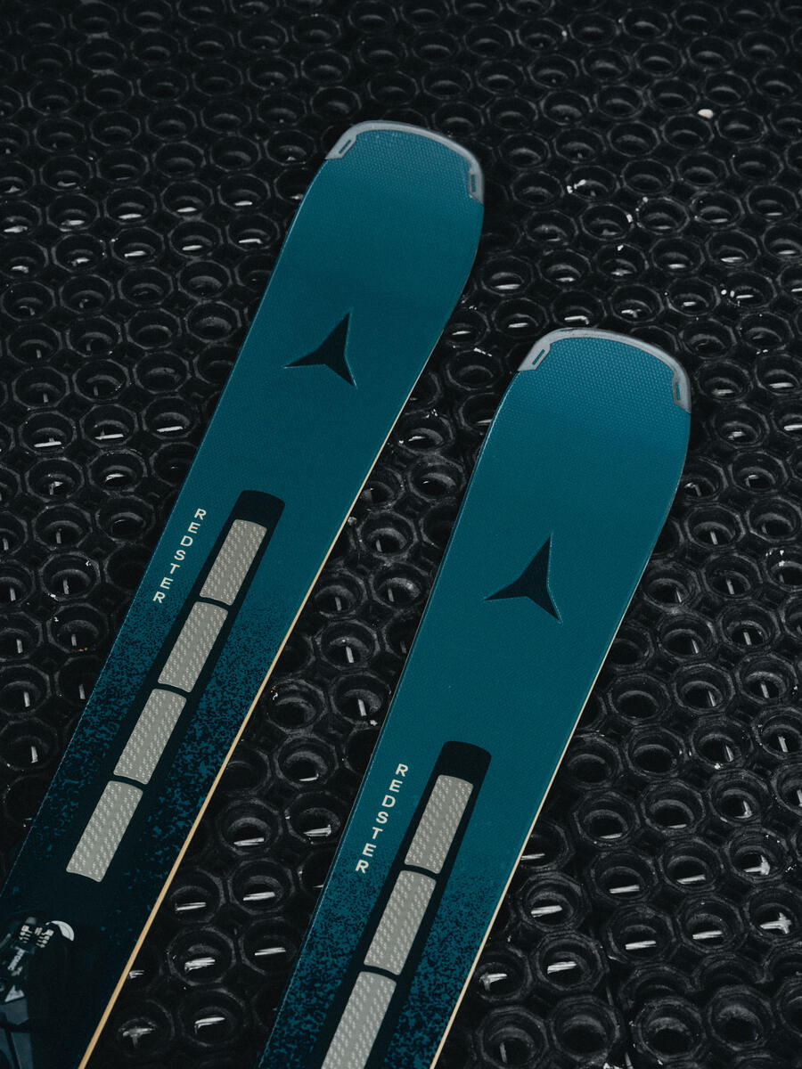 Two teal and black ski tips with a dark triangular logo and vertical 'SAPIR' branding, laid diagonally on a black textured circular surface.