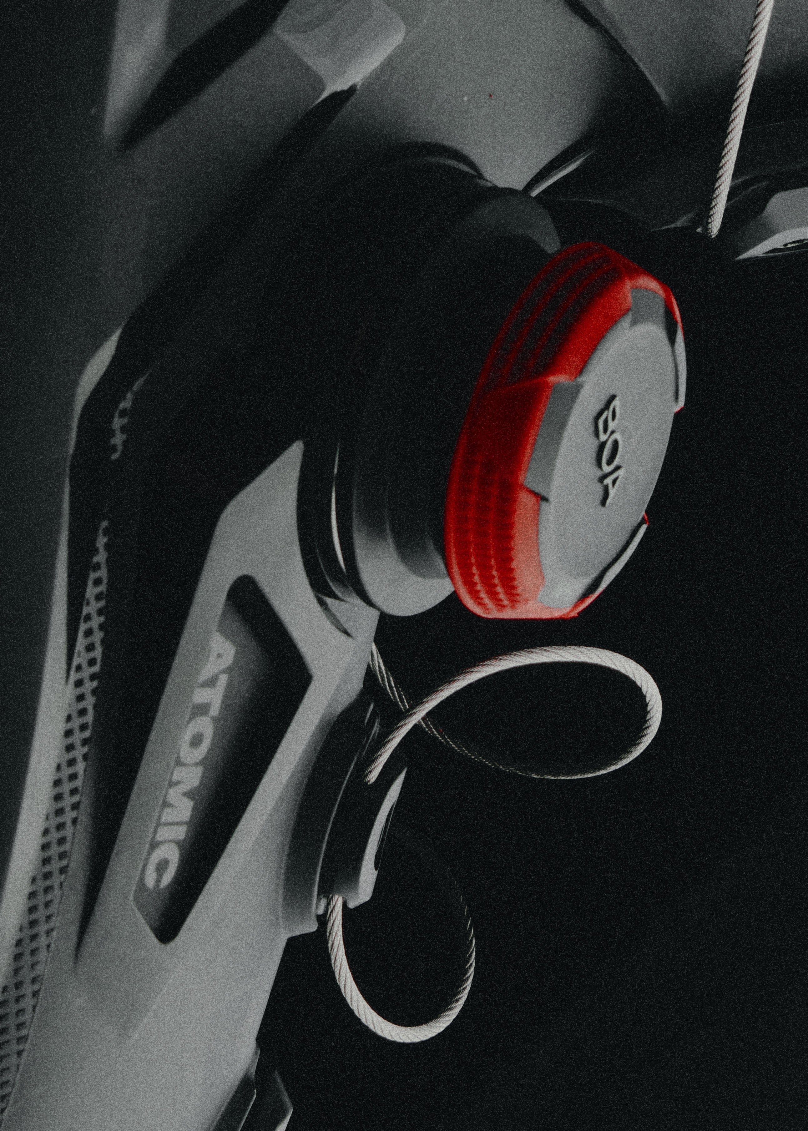 A close-up of a black and gray bicycle handlebar component with a bright red circular accent and a silver cable loop, set against a dark background. The word 'ATOMIC' is visible on the handlebar.