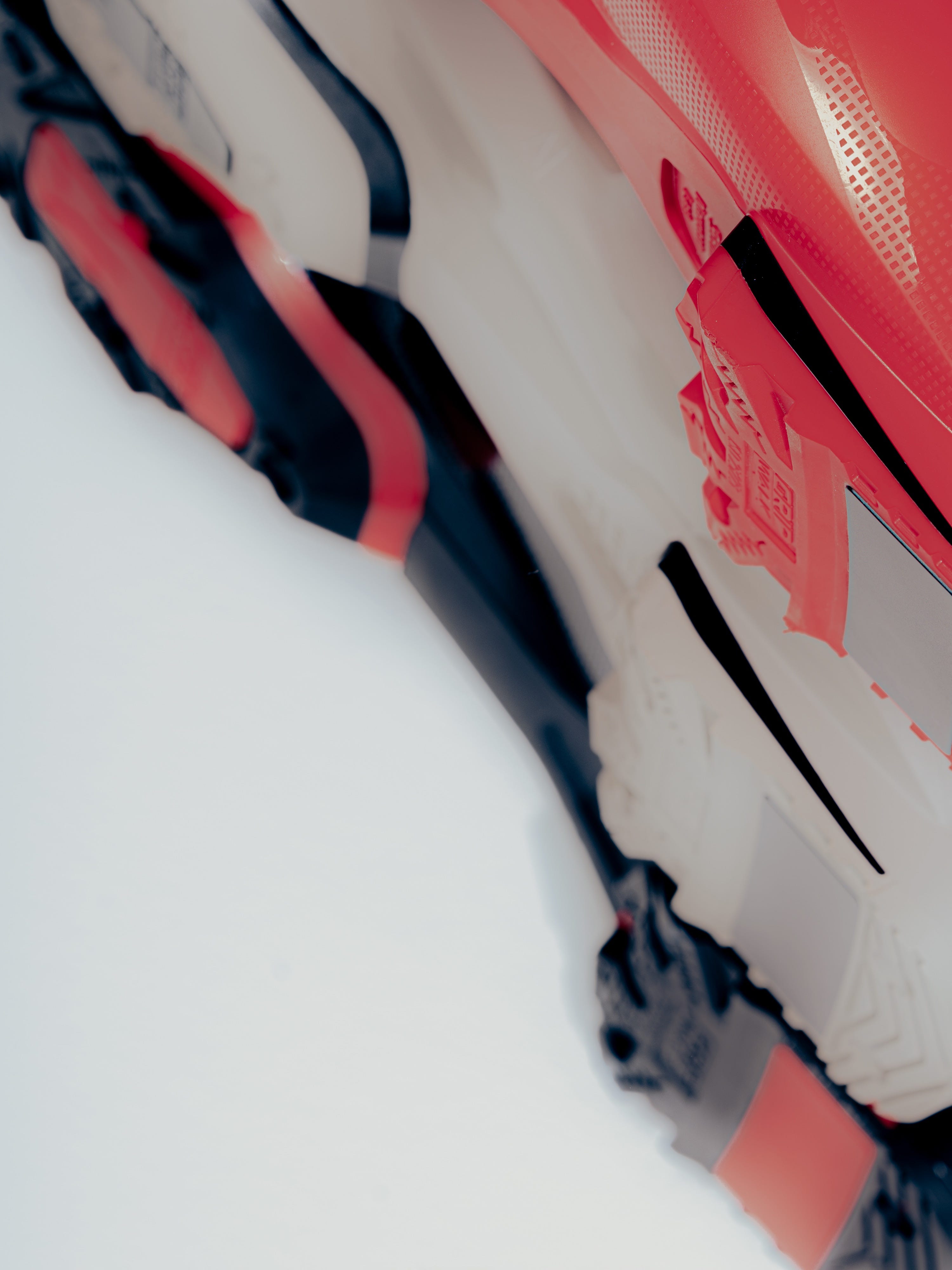 A close-up angled view of a red, black, and white technical boot or snowboard boot with textured panels and a lace-up closure on a white background.