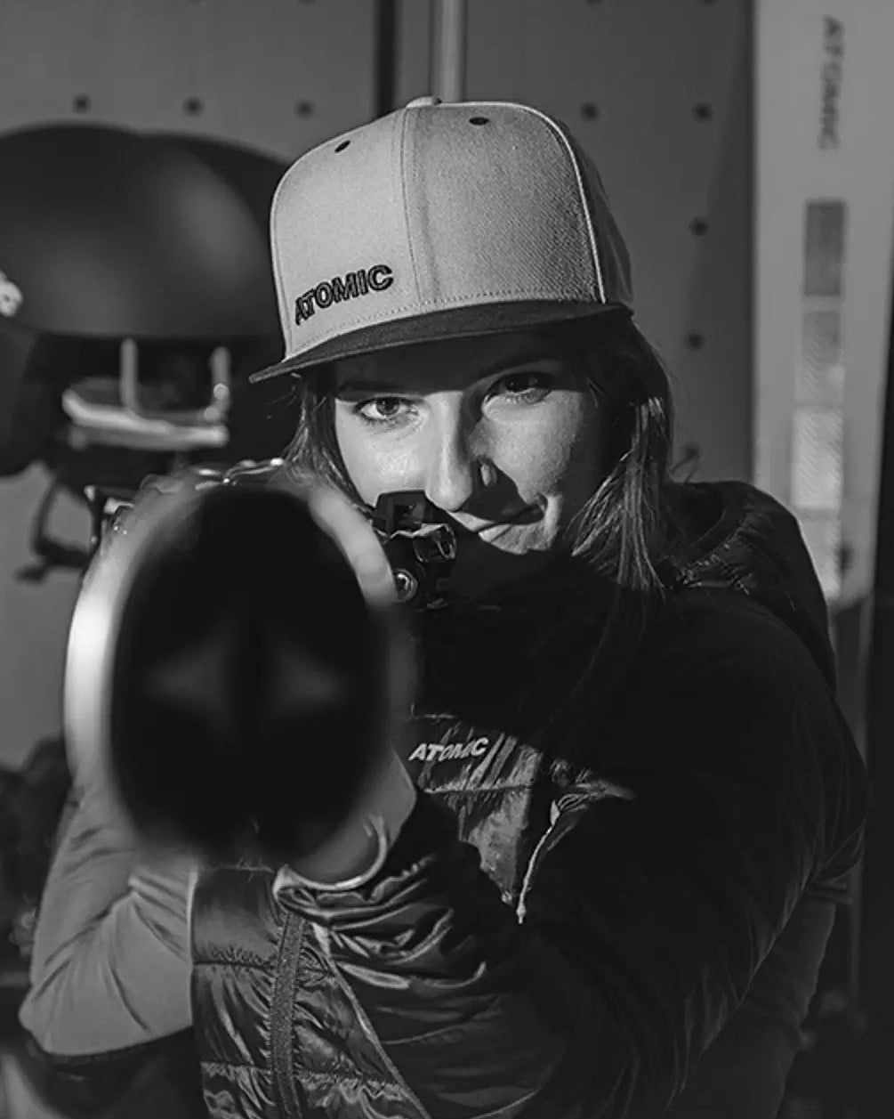 A black and white lifestyle photograph of Maryna Gasienica-Daniel wearing an Atomic brand cap and jacket with a skis on her hands.