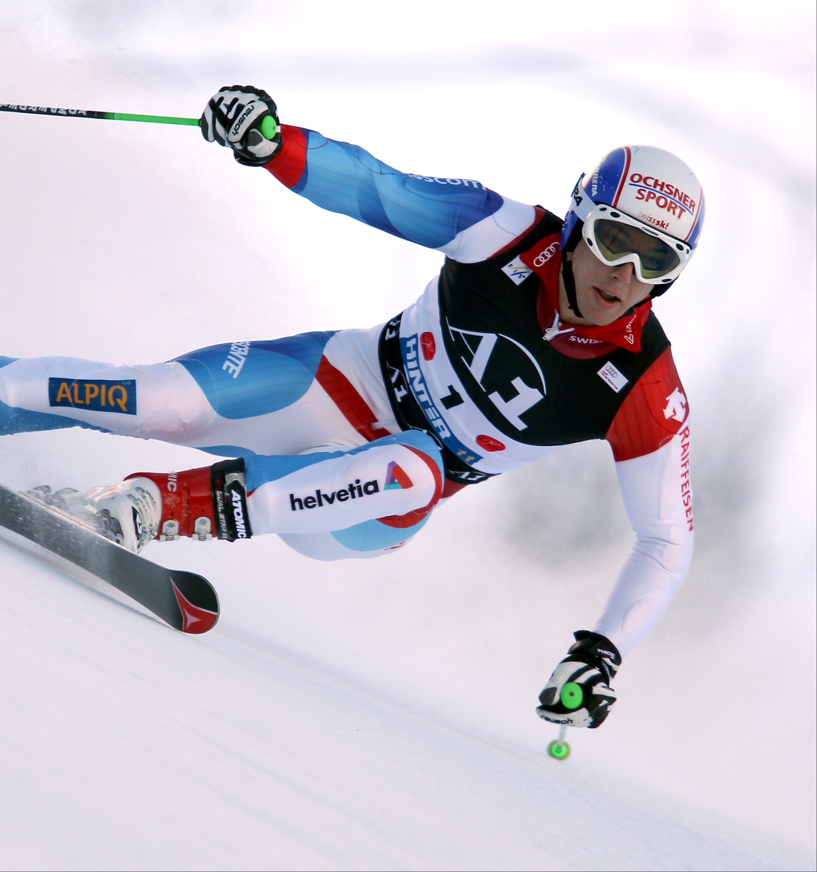 Carlo Janko in a blue, white, and red racing suit carving through snow, with visible logos.