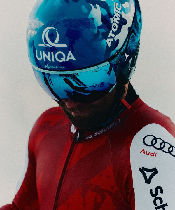 A close-up of Marco Schwarz wearing a red and white ski suit with visible logos, along with a blue reflective helmet and visor.