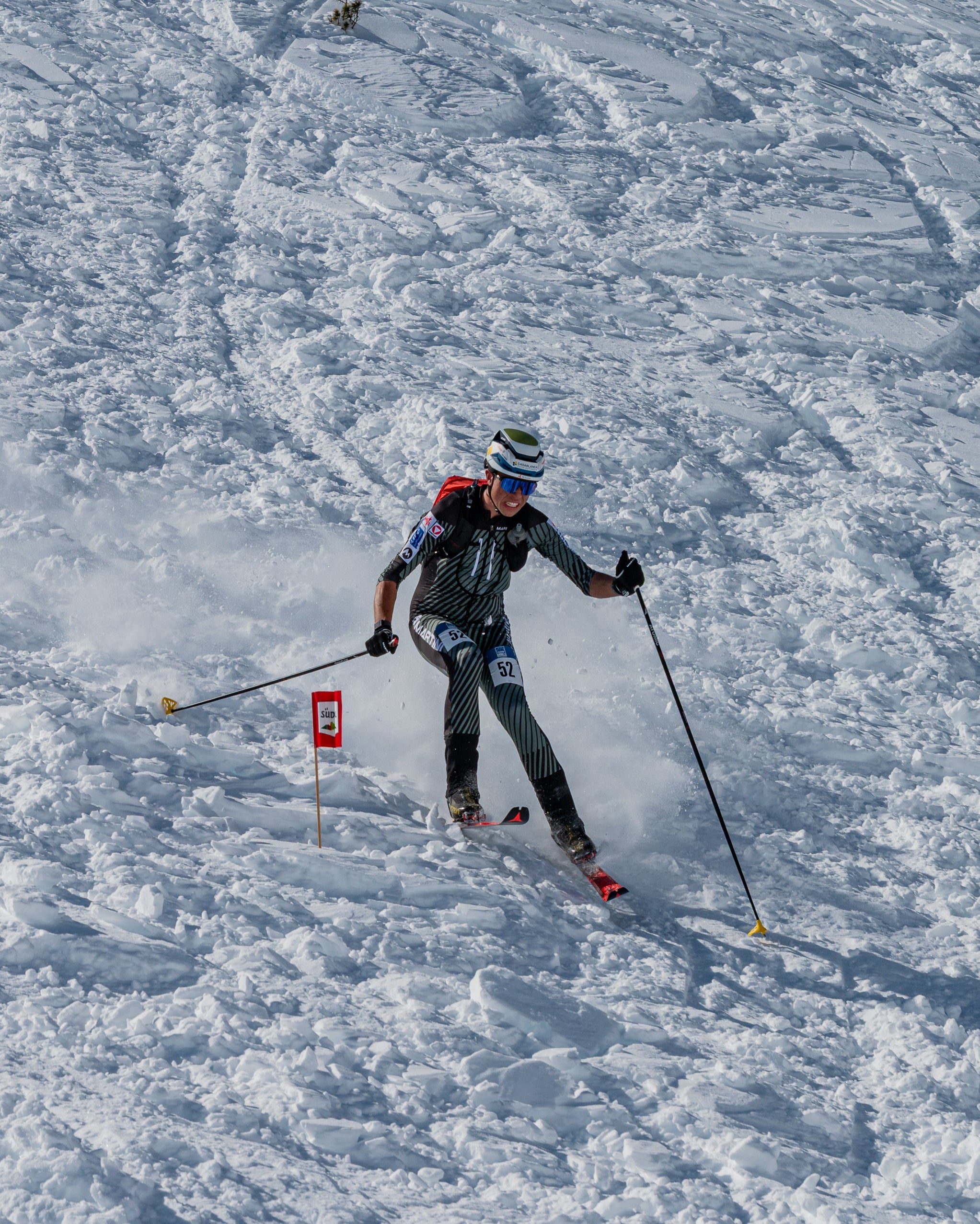 SIlvano Wolf carving through deep snow on a sunny mountain slope, wearing a dark ski suit, touring helmet, and holding ski poles.