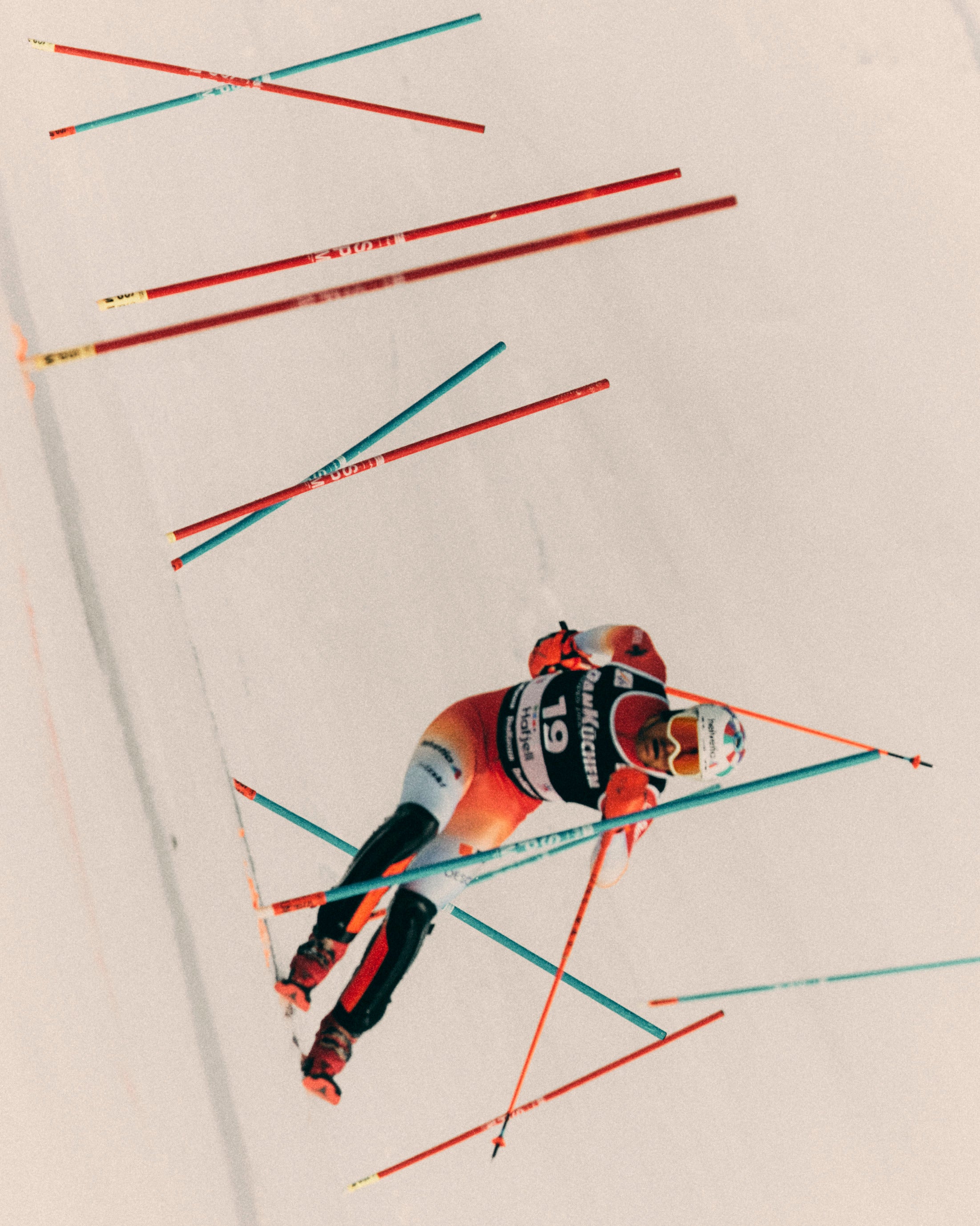 Daniel Yule in a red, black, and white racing suit navigates a slalom course with red and blue poles on a snowy white background.