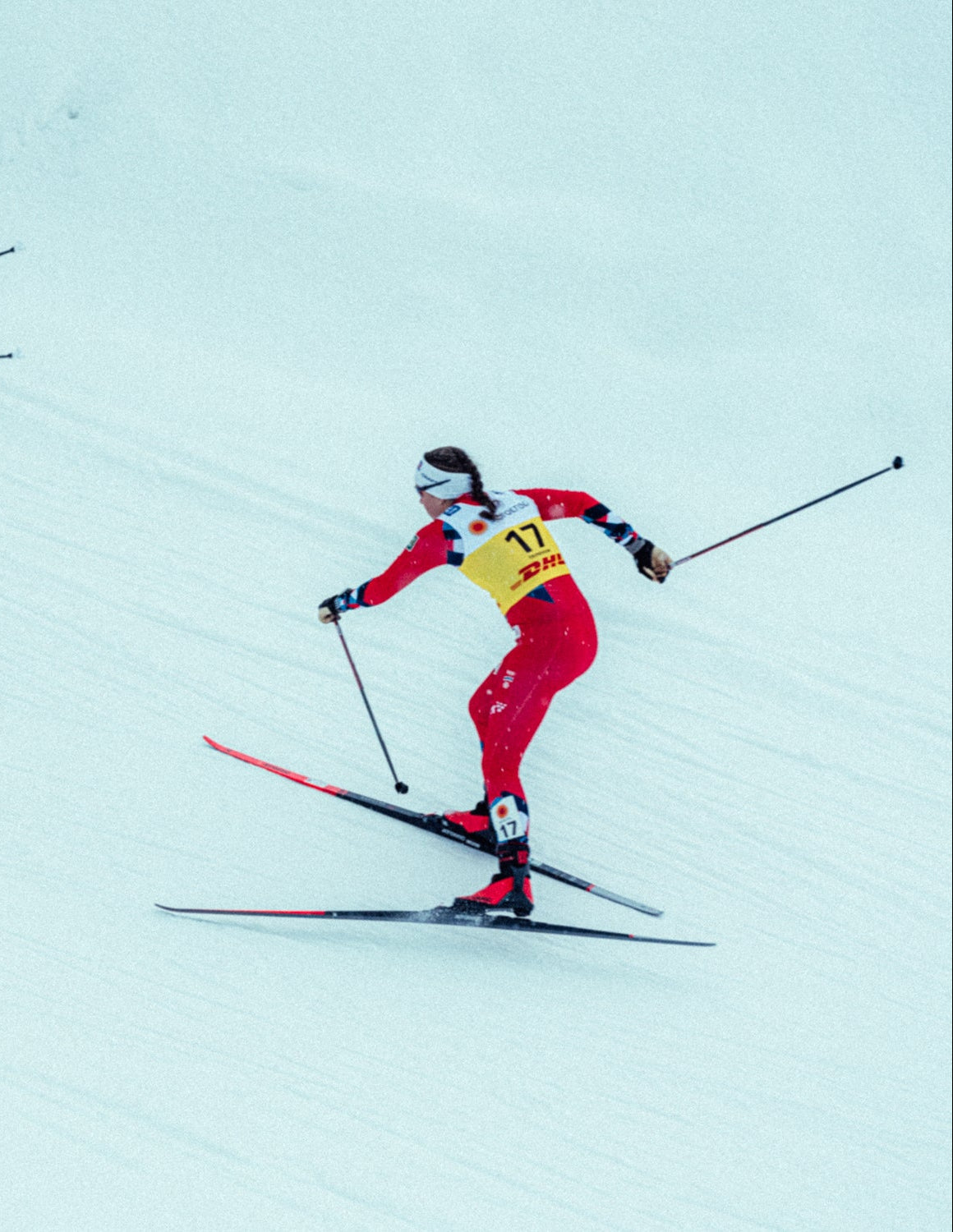 Lotta Udnes Weng moving across a snowy slope in a red and yellow suit, holding ski poles.