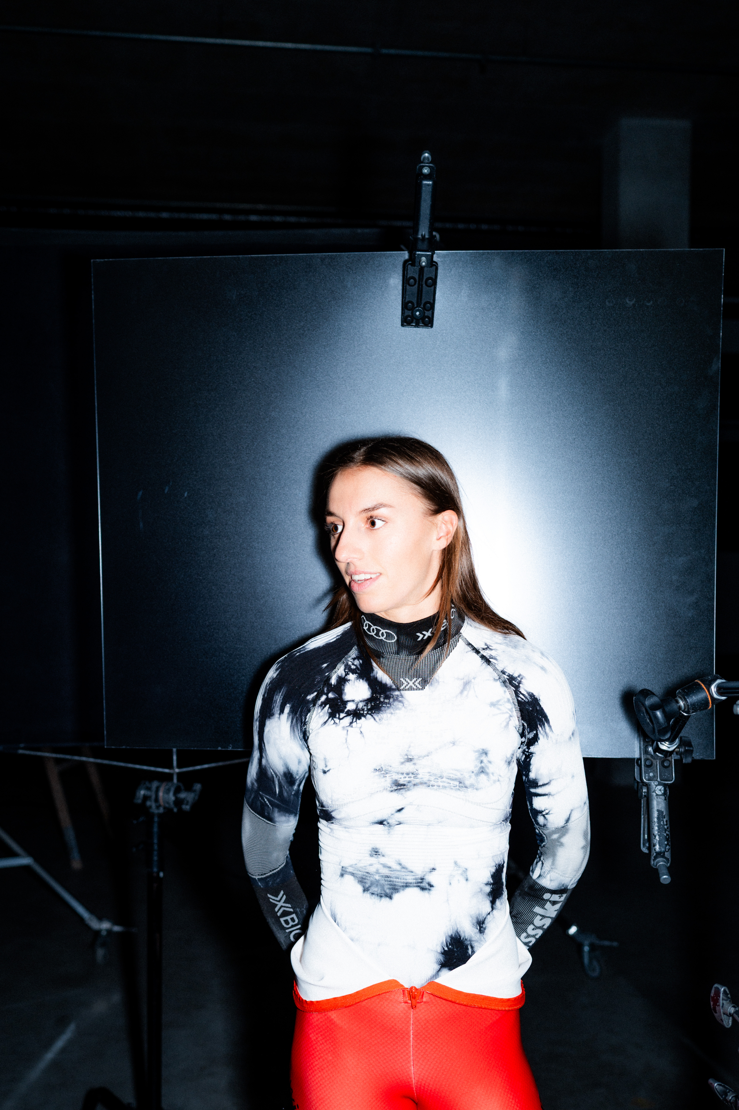 Malorie Blanc wearing a black and white abstract patterned long-sleeve top and bright red athletic leggings stands in a studio setting.