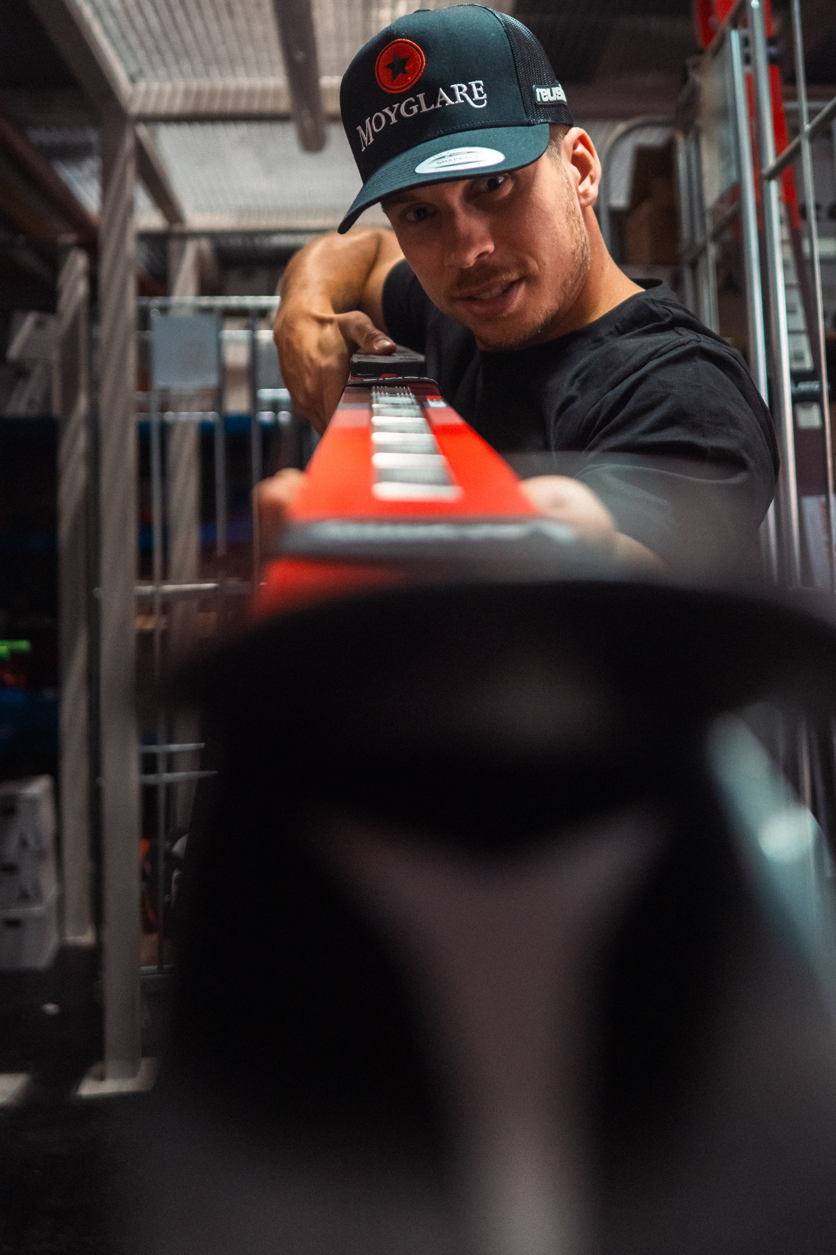 Gino Cavizel wearing a black Moynage baseball cap and black t-shirt holds a red ski.