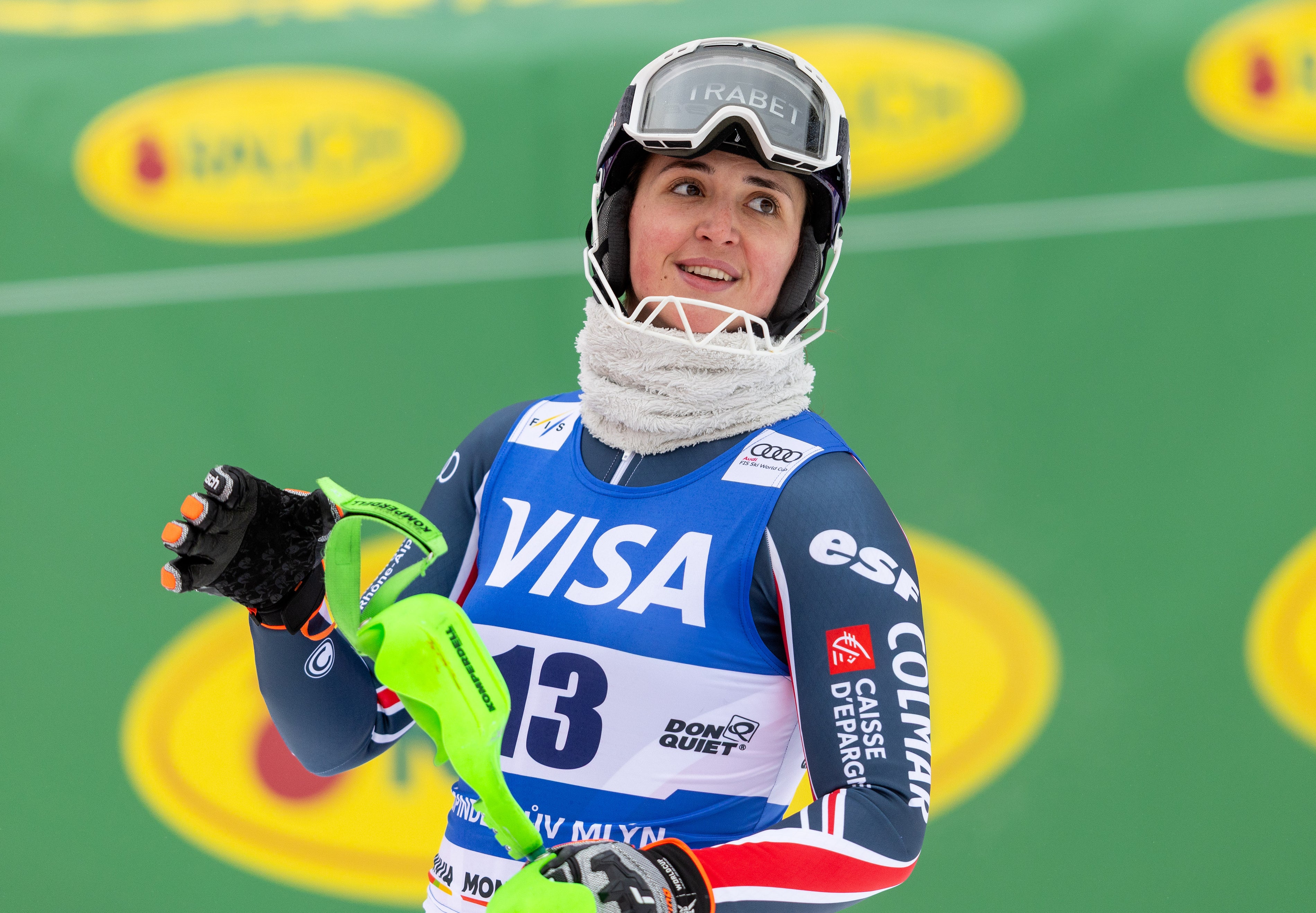Chevrier Marion in a blue and white racing suit with sponsor logos like Visa and Esports, wearing a helmet and goggles, holding a bright green towel on a green track.