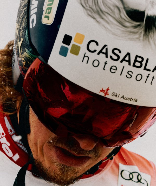 Close-up of Manuel Feller wearing a black helmet with a white sponsor sticker reading 'CASABLA hotelsoft' and red mirrored ski goggles.