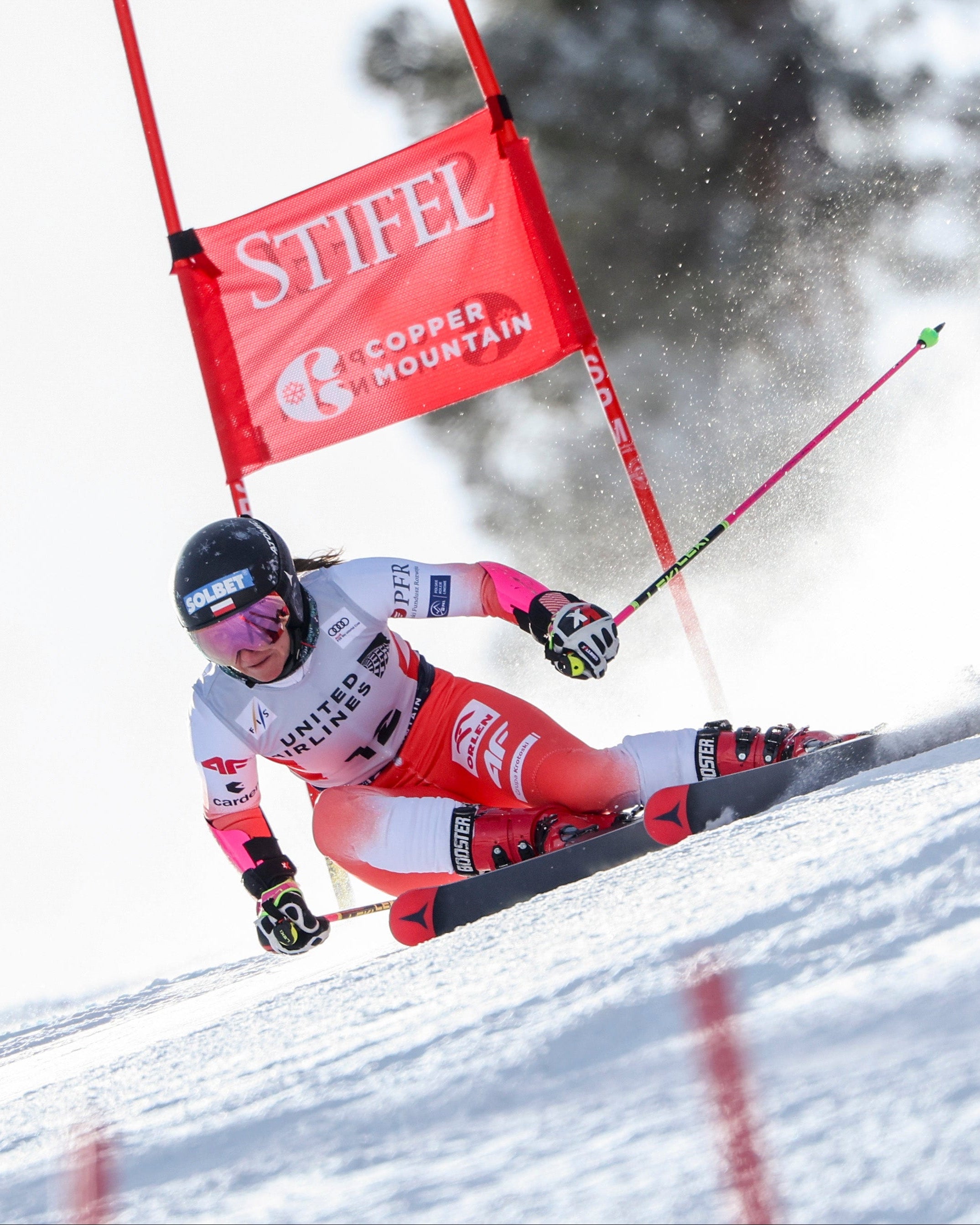 Maryna Gasienica-Daniel in a red and white racing suit navigates a snowy slope during a slalom race, passing a red gate.