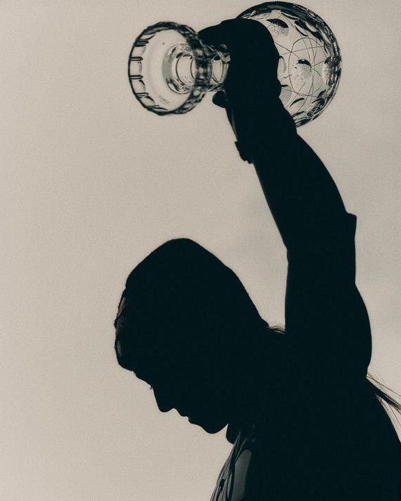 A high-contrast silhouette of a person holding a clear crystal globe  above her head against a plain light background.