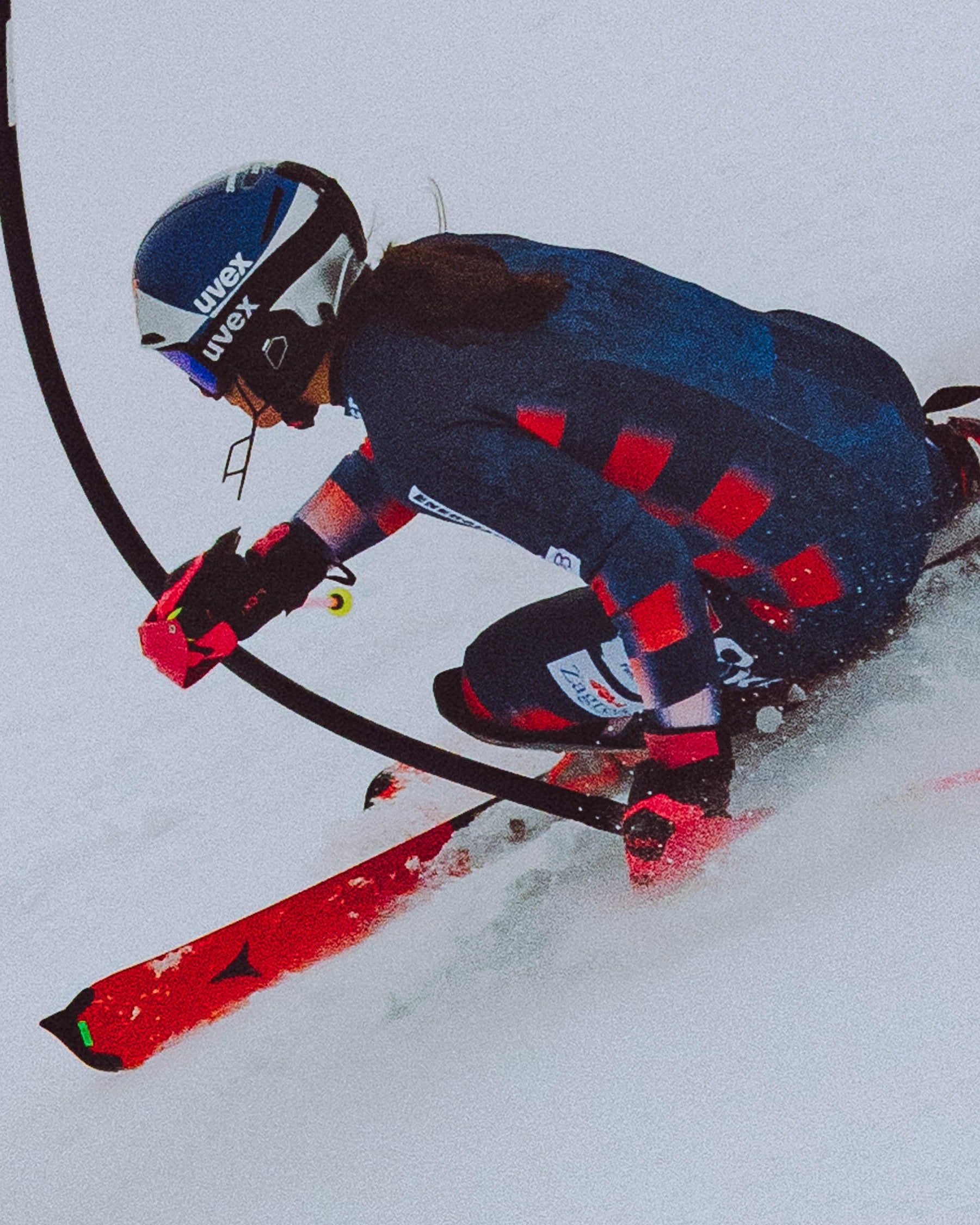 Zrinka Ljutic carving through the race course, wearing a dark blue and red checkered racing suit, a blue helmet and red skis.