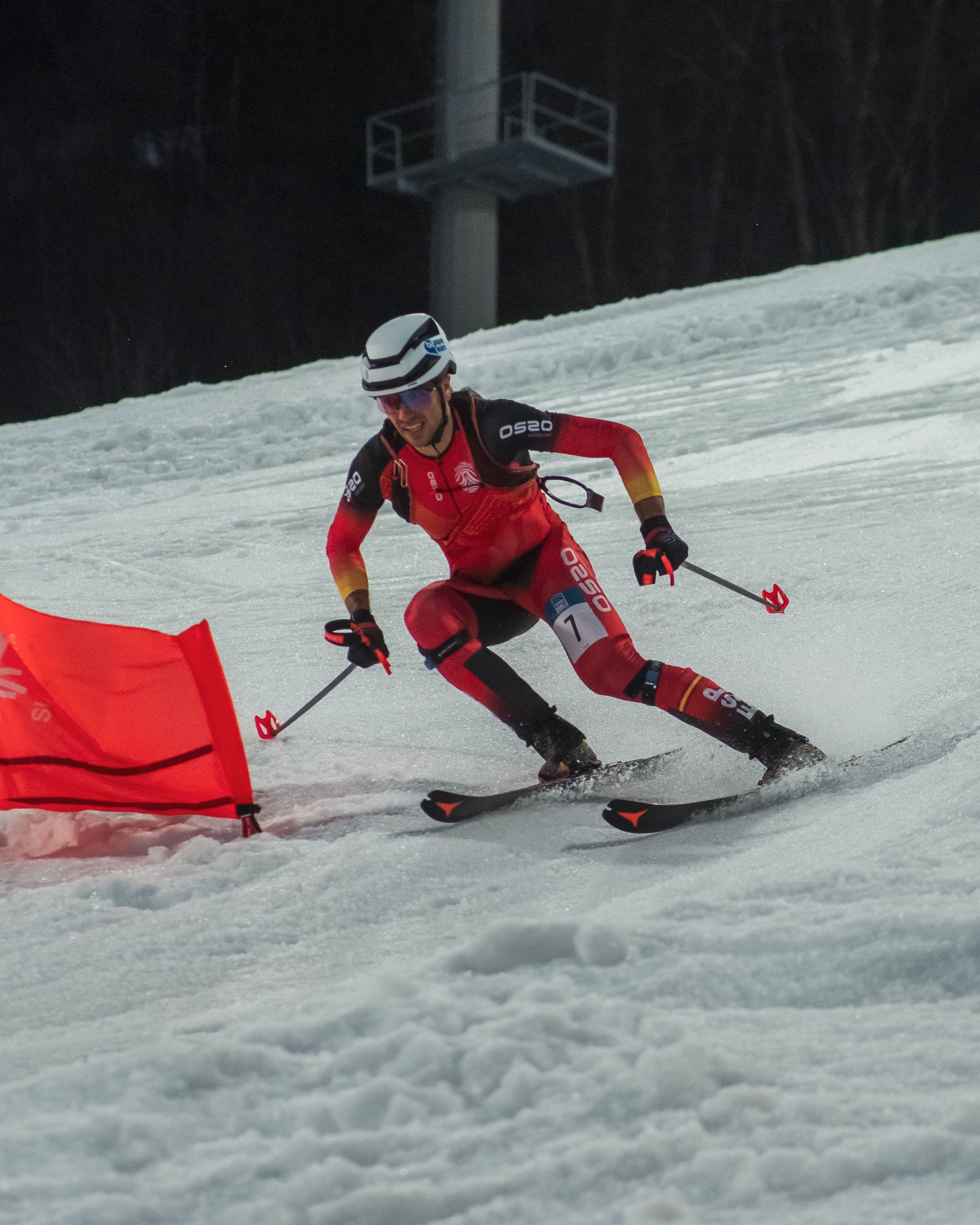 Íñigo Martínez de Albornoz in a red and black racing suit navigates a snowy slope around a bright red gate, with a blue gate visible in the background.