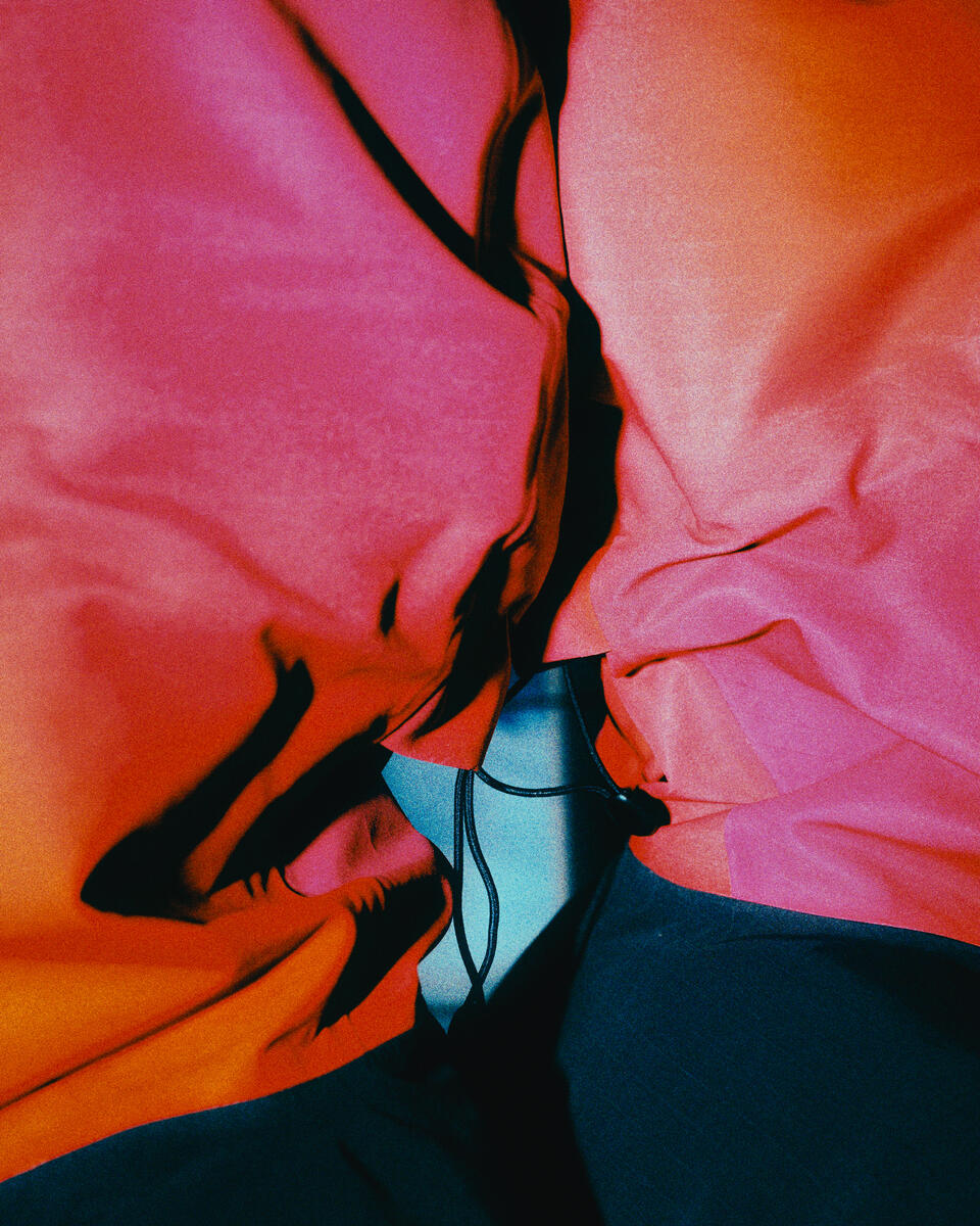 A close-up of a garment with draped fabric in bright pink, orange, and dark navy, with a small light blue section and black trim details.