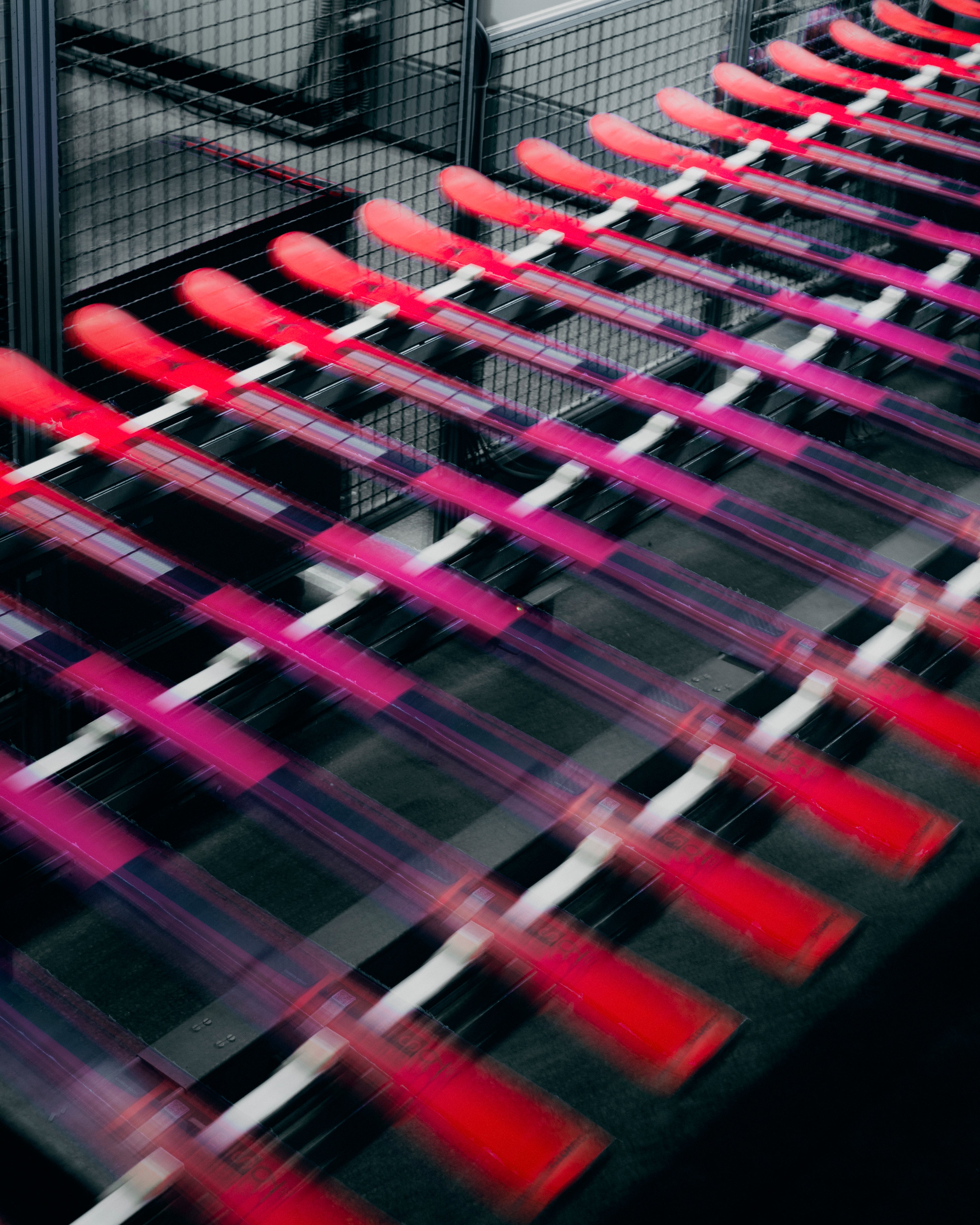A dynamic, motion-blurred close-up of multiple red and pink cylindrical items arranged diagonally on a dark conveyor belt or rack system.