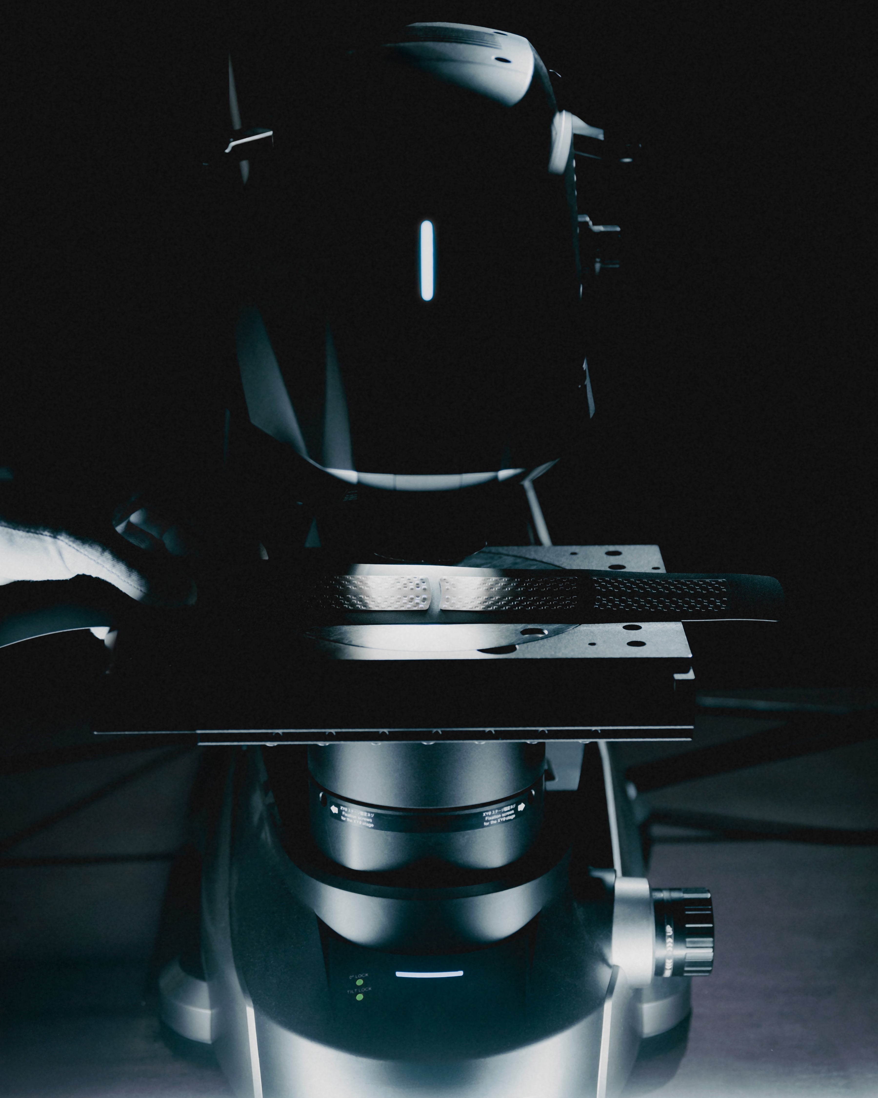 A close-up, dramatic studio shot of a dark metallic scientific machine component against a nearly black background, with cool blue highlights and no visible people or real environment.