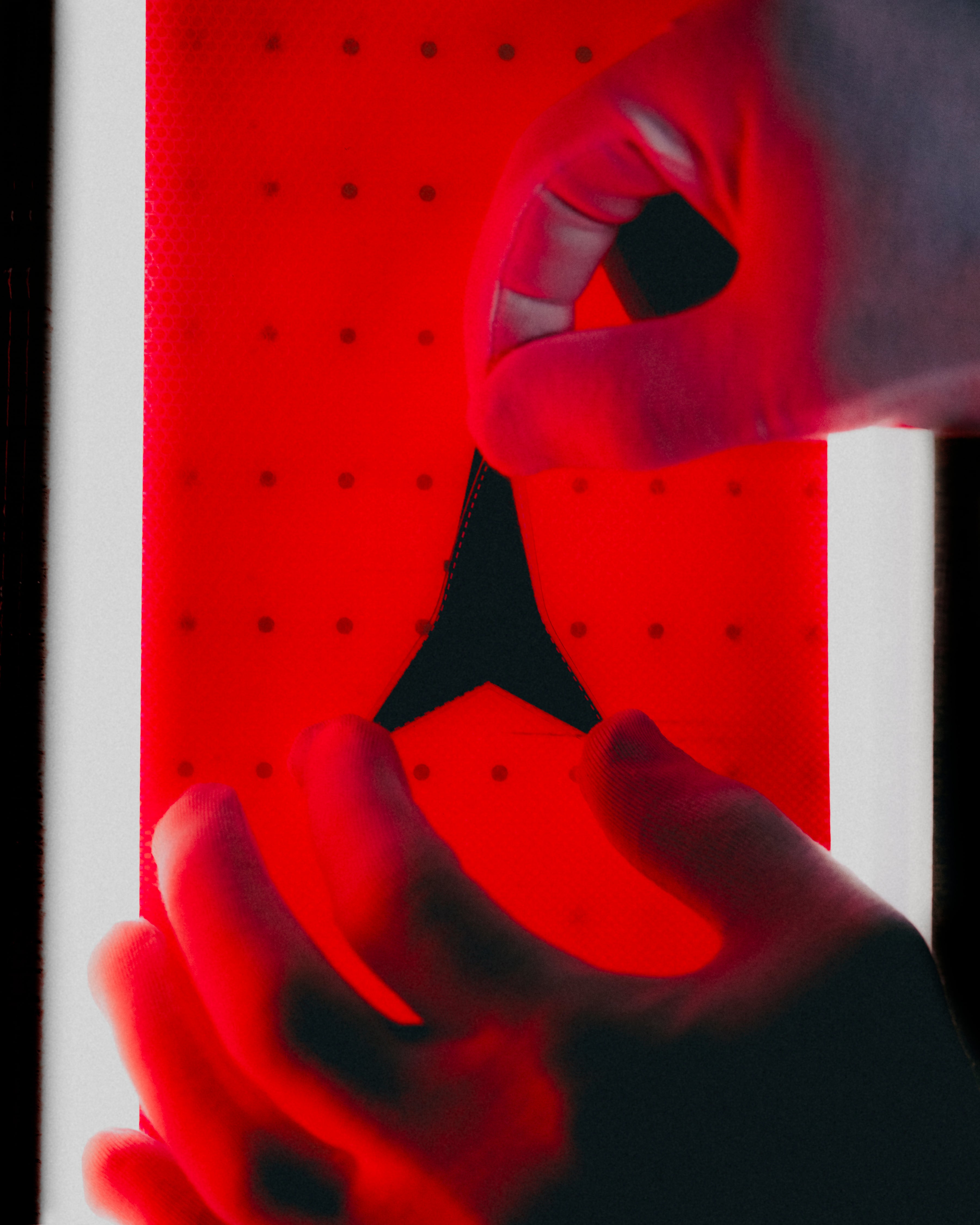 A close-up of two hands applying a black triangular adhesive patch to a red perforated backing board.