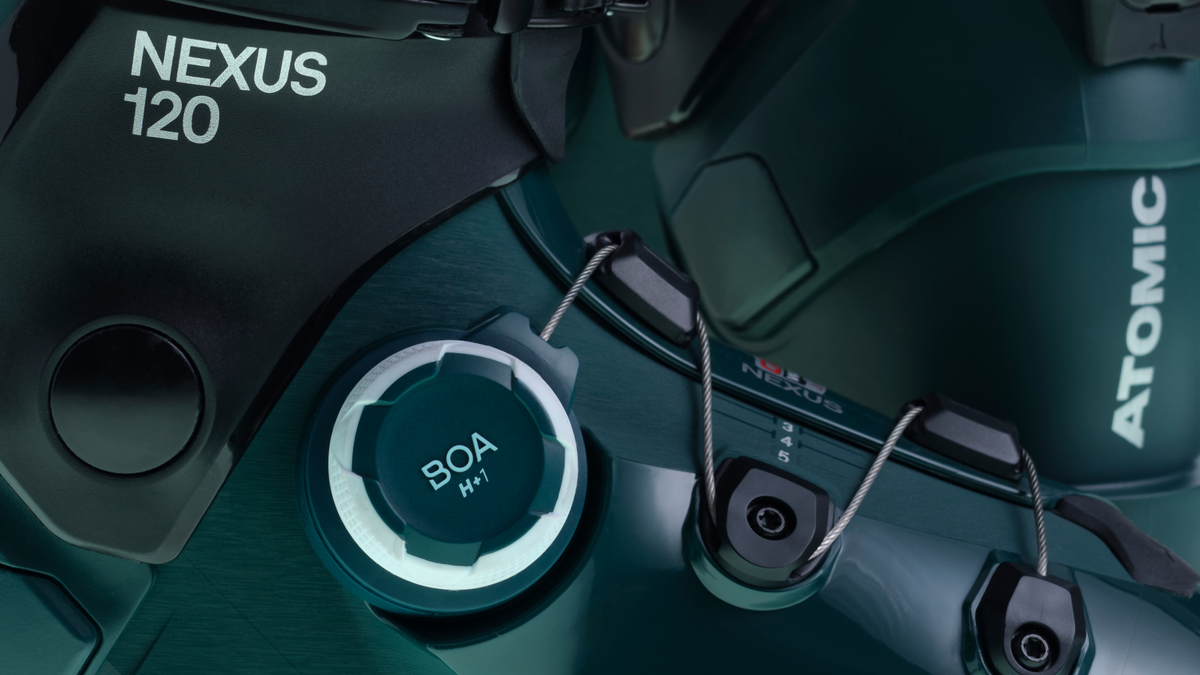 Close-up of a dark teal and black gaming headset, showing the 'NEXUS 120' model name, 'BOA' tension adjustment system cap, and 'ATOMIC' earcup branding.