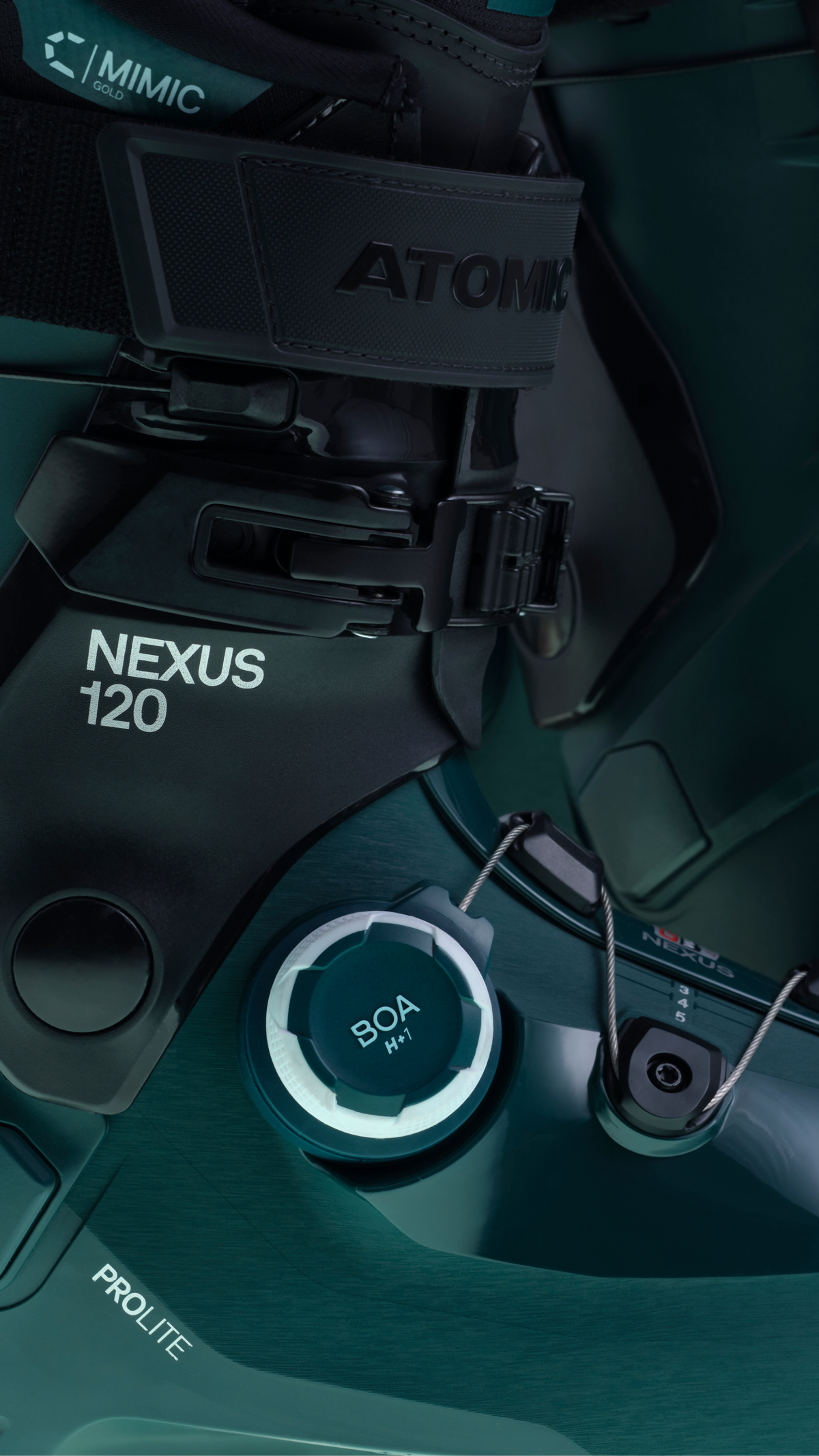 Close-up of a dark teal and black snowboard binding system with visible branding including ATOMIC, NEXUS 120, and BOA 900. The photo shows hardware, straps, and adjustment components arranged on the board surface.