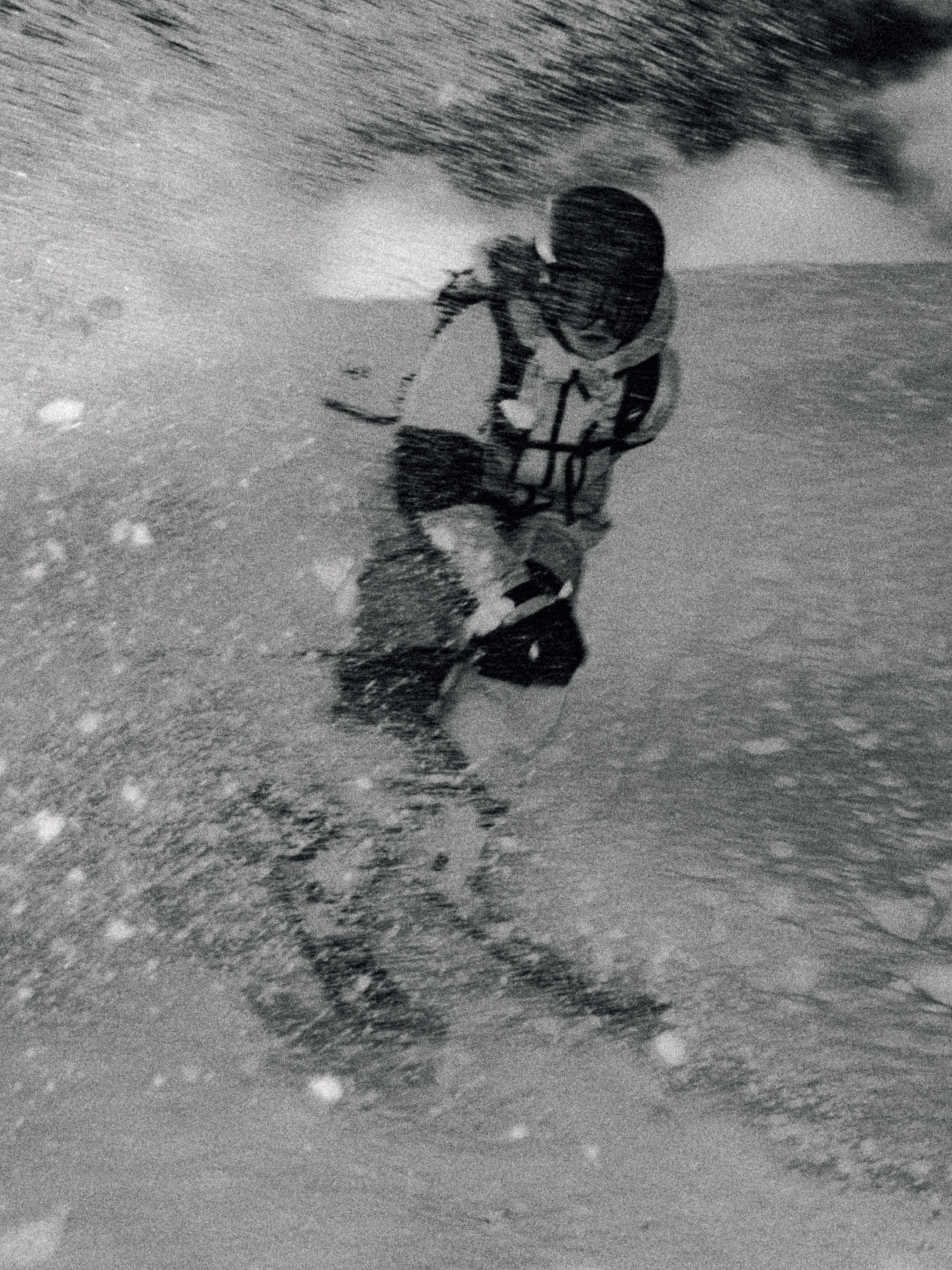 Black and white action photograph of a skier carving through heavy snow spray, wearing a helmet, goggles, and a ski jacket.
