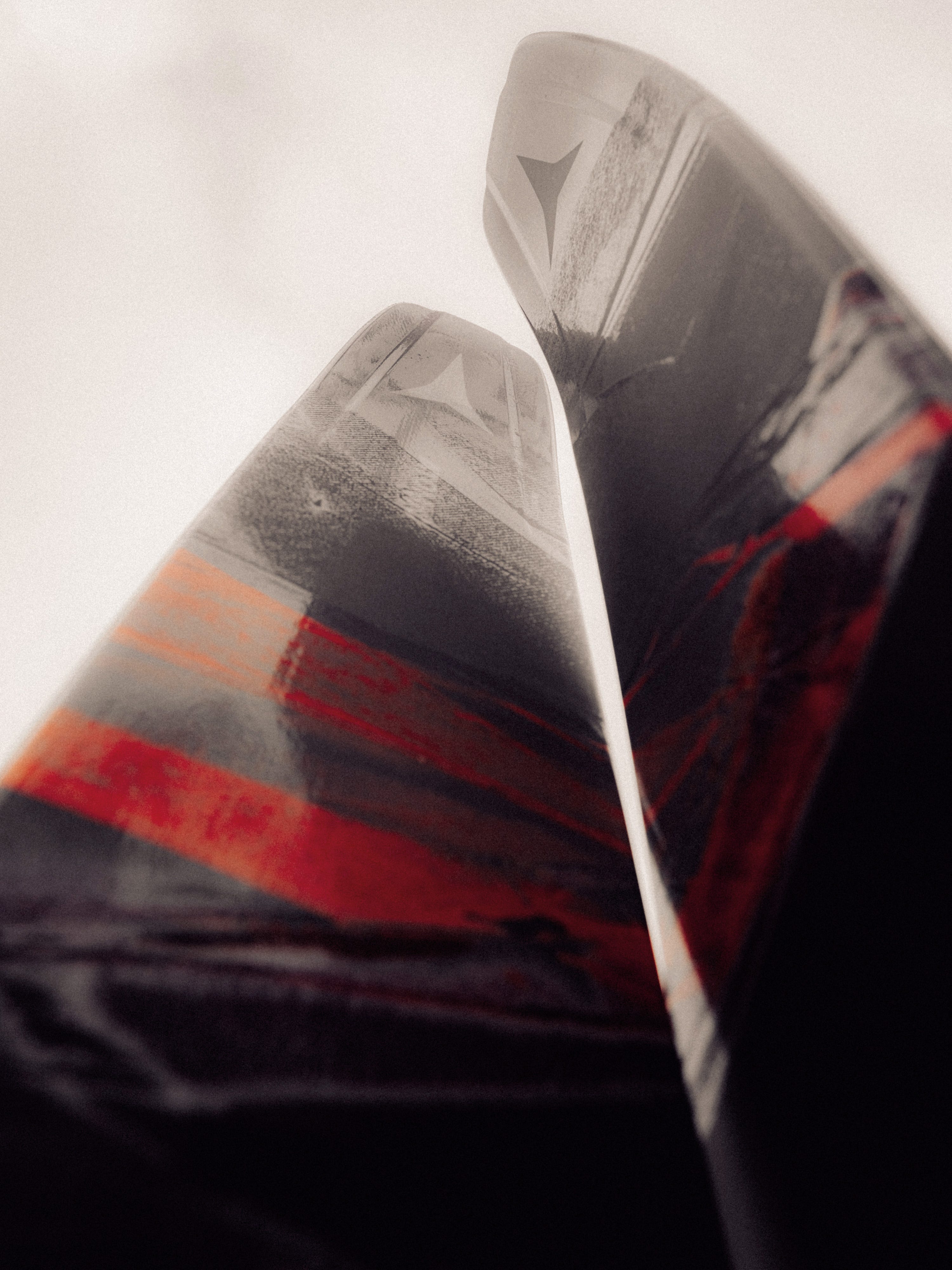 Close-up of two glossy ski  tails with a black, gray, and red abstract design, photographed against a bright overcast sky.