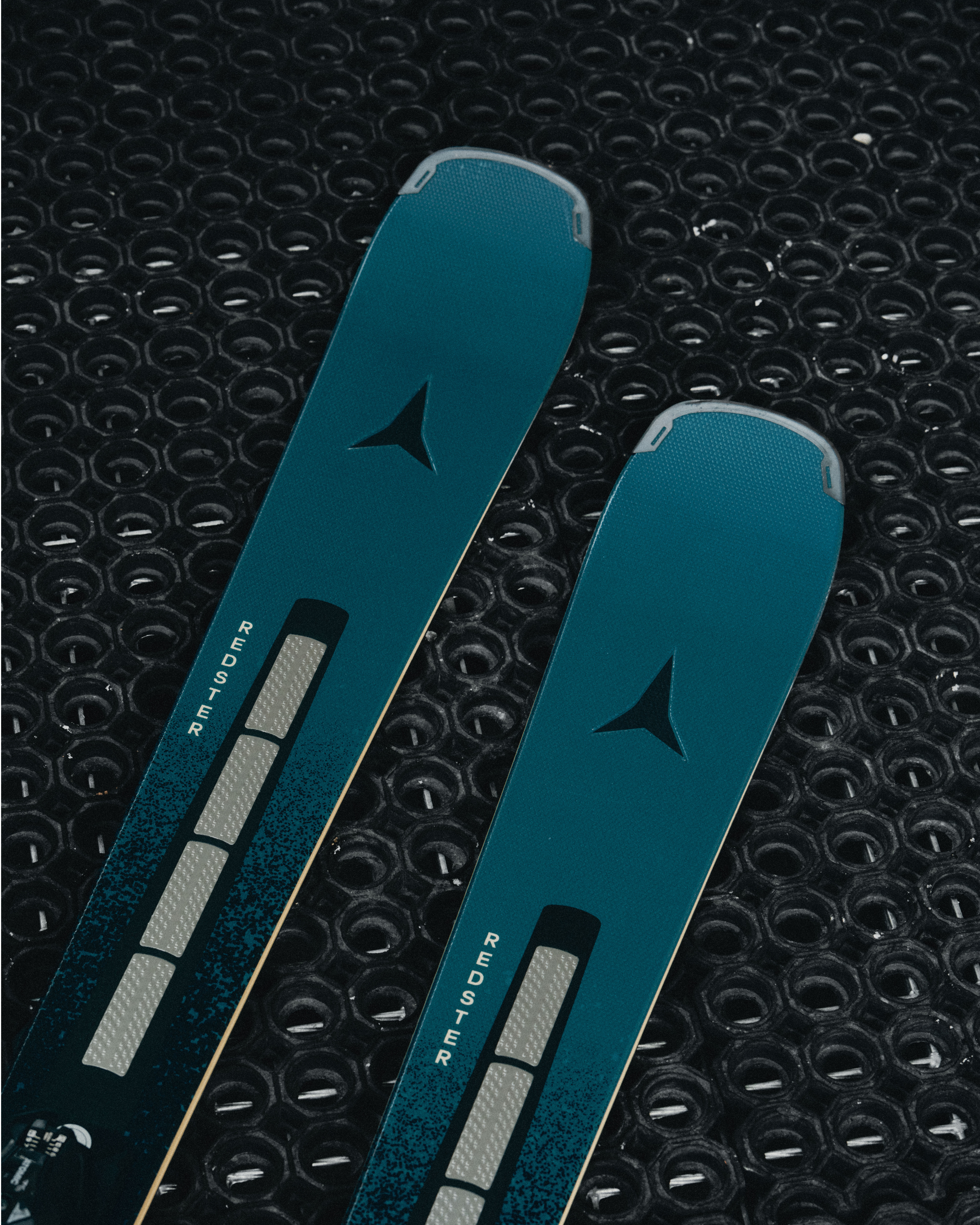Close-up of two teal-blue skis with black triangular logos and white 'sequoia' branding, placed diagonally on a black textured surface.
