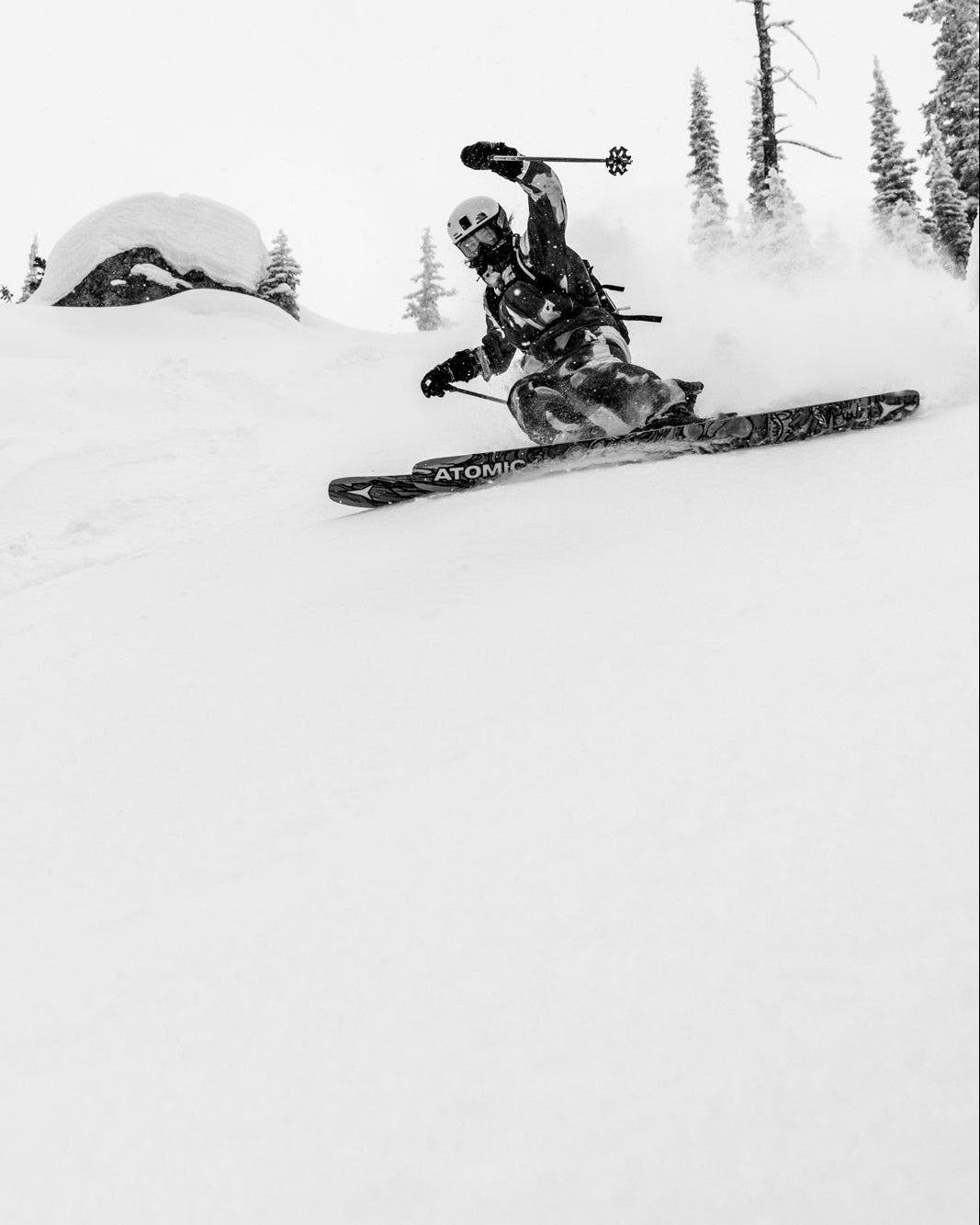 Janelle Yip carving through deep powder snow, with other snowboarders and skiers visible in the background on a snowy mountain slope.