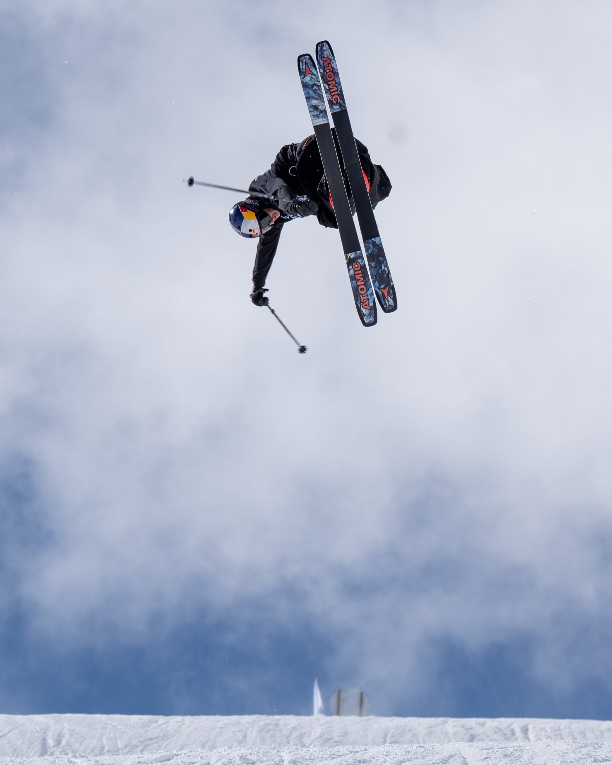 Nico Porteous performing an air trick on a snowy mountain under a blue sky with white clouds.