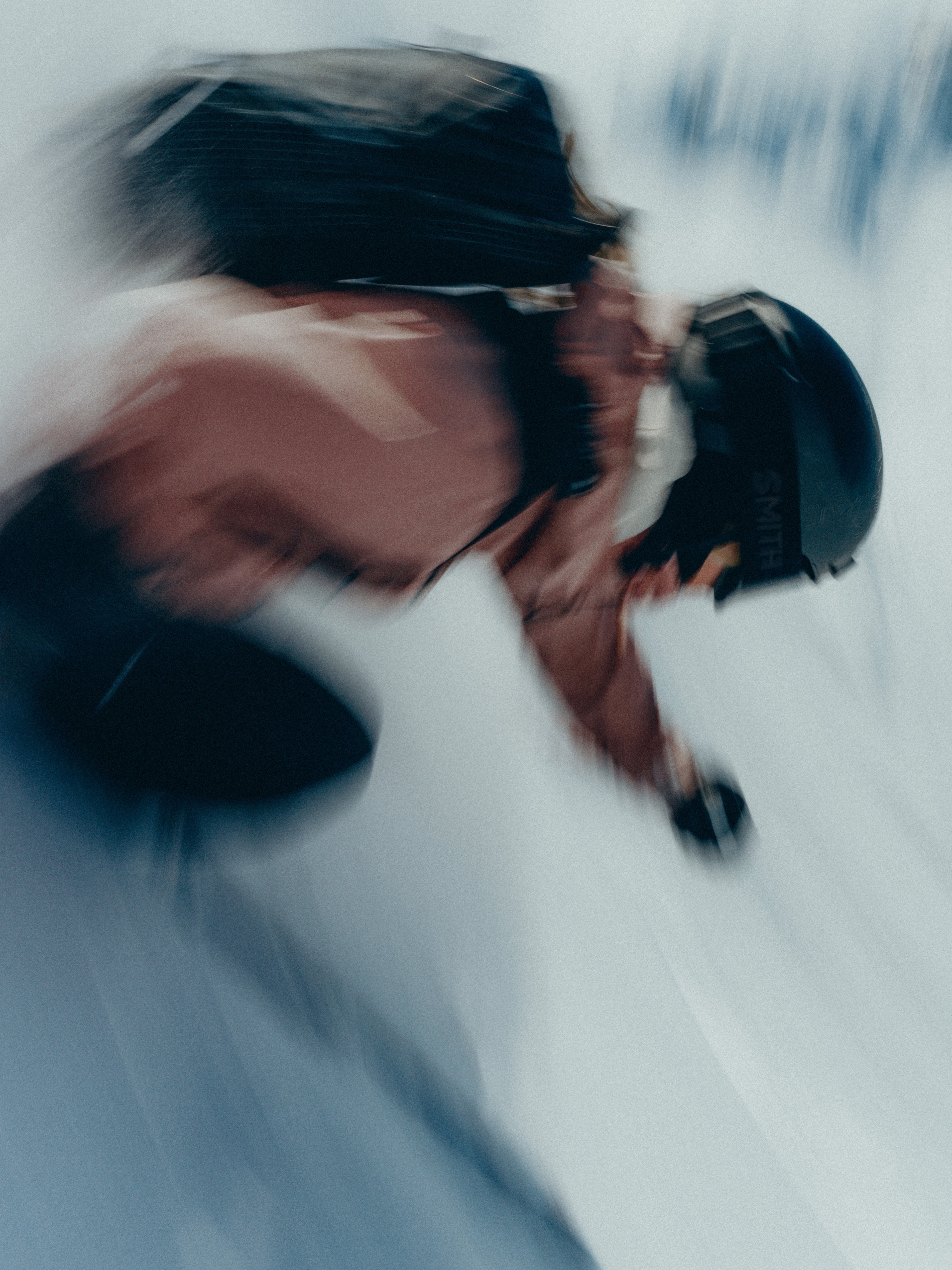 Tonje Kvikik in motion wearing a black helmet and backpack, captured with a dynamic motion blur effect against a snowy white background.