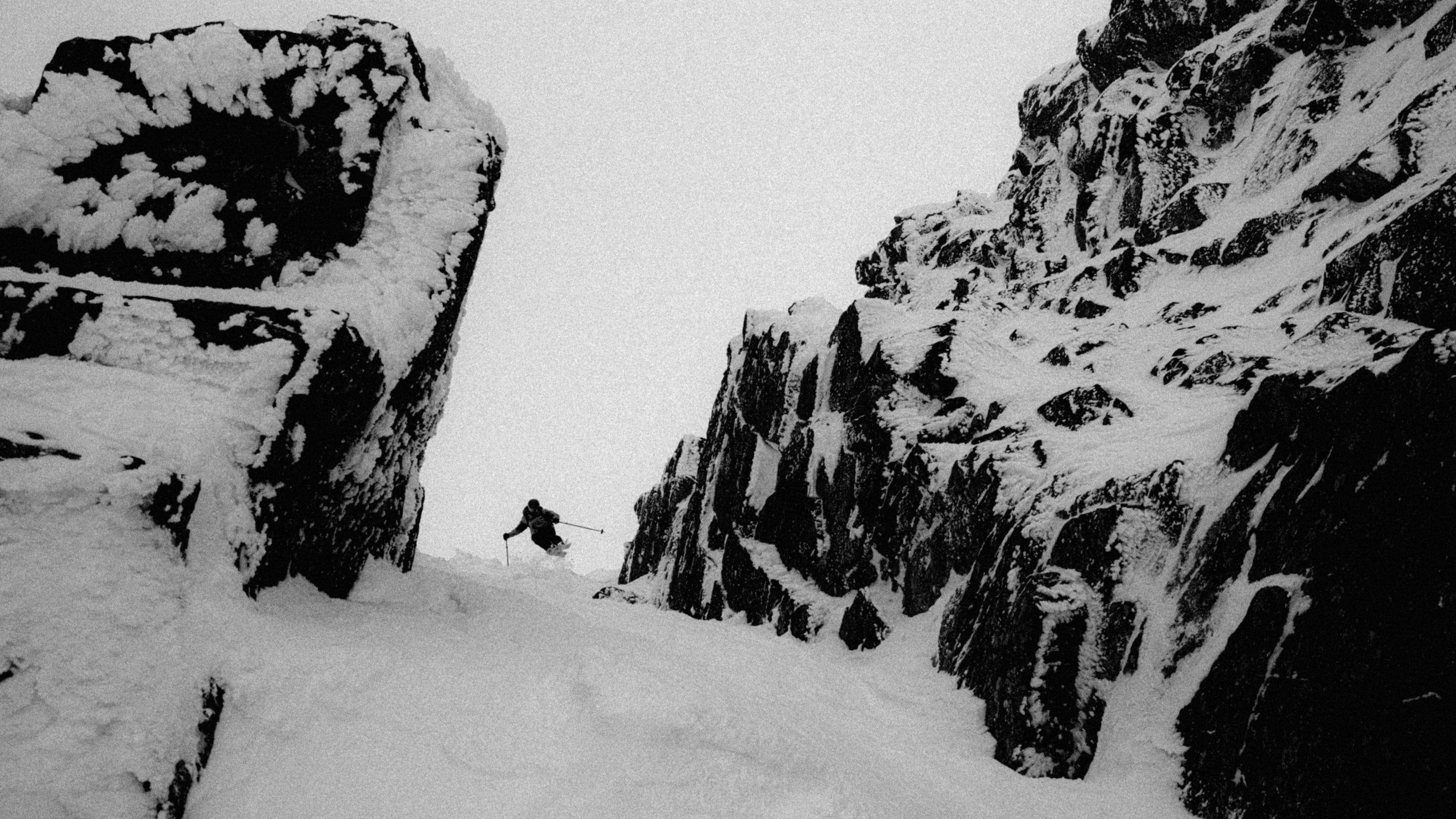 Black and white photograph of Christopher Rubens navigating a snowy mountain pass between steep, snow-dusted rock cliffs.