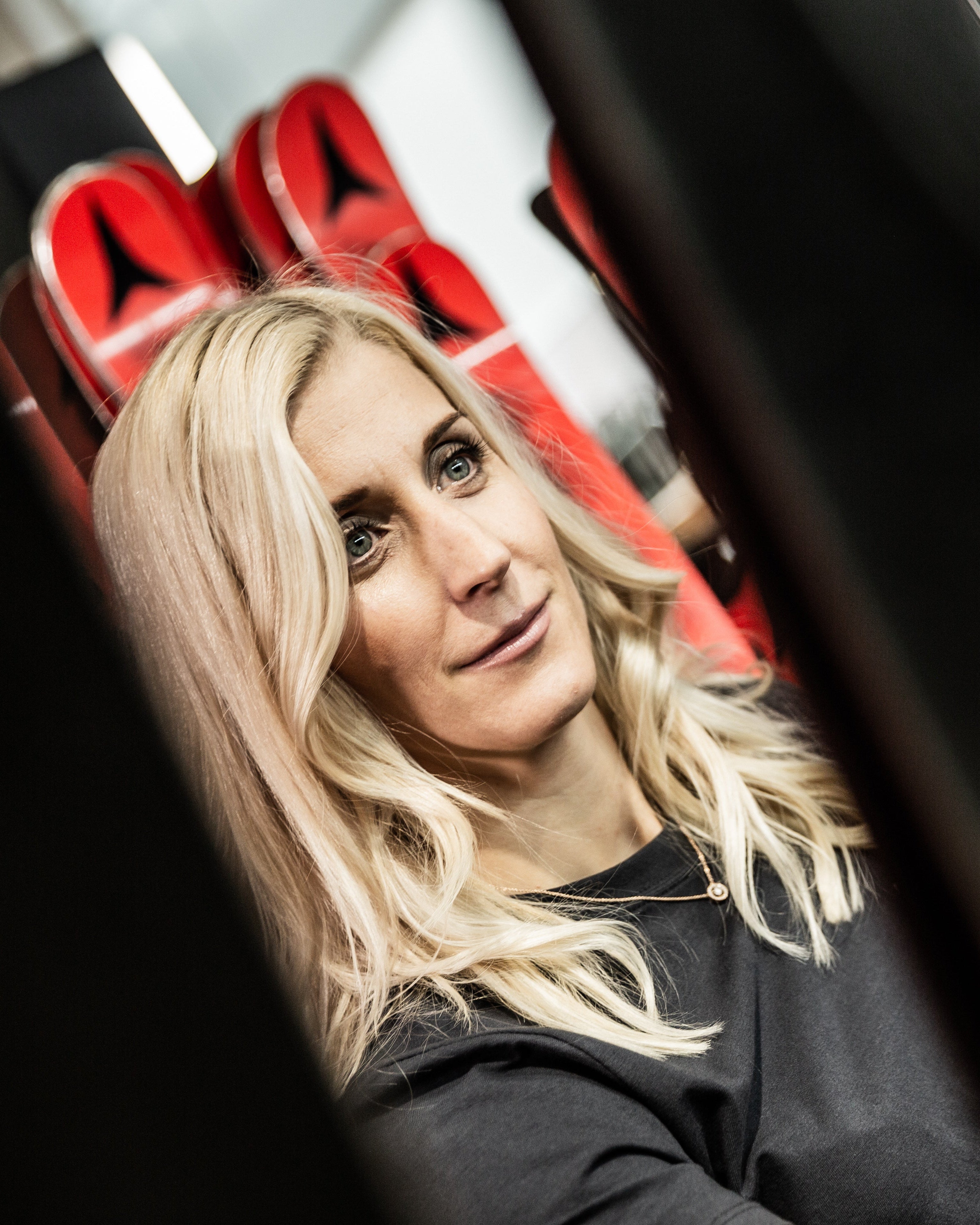 Eva Maria Braem in a black top looks over her shoulder in a ski storage area with red and black skis in the background.